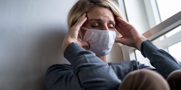 Woman with face mask indoors at home feeling stressed, mental health and coronavirus concept.