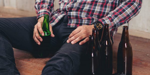 Alcohol addicted handsome man sitting alone with alcohol bottle