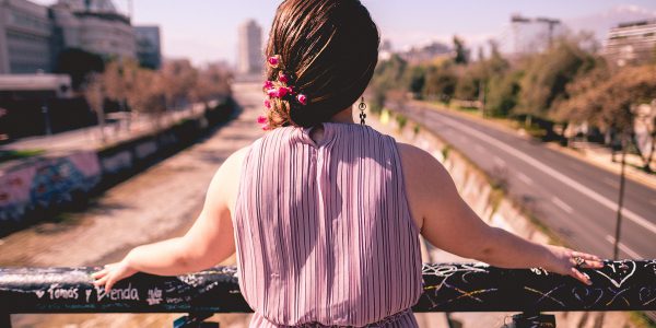 Girl from back with purple dress and beautiful braided hair with flowers in front of Mapocho river and Santiago cityscape, Chile
